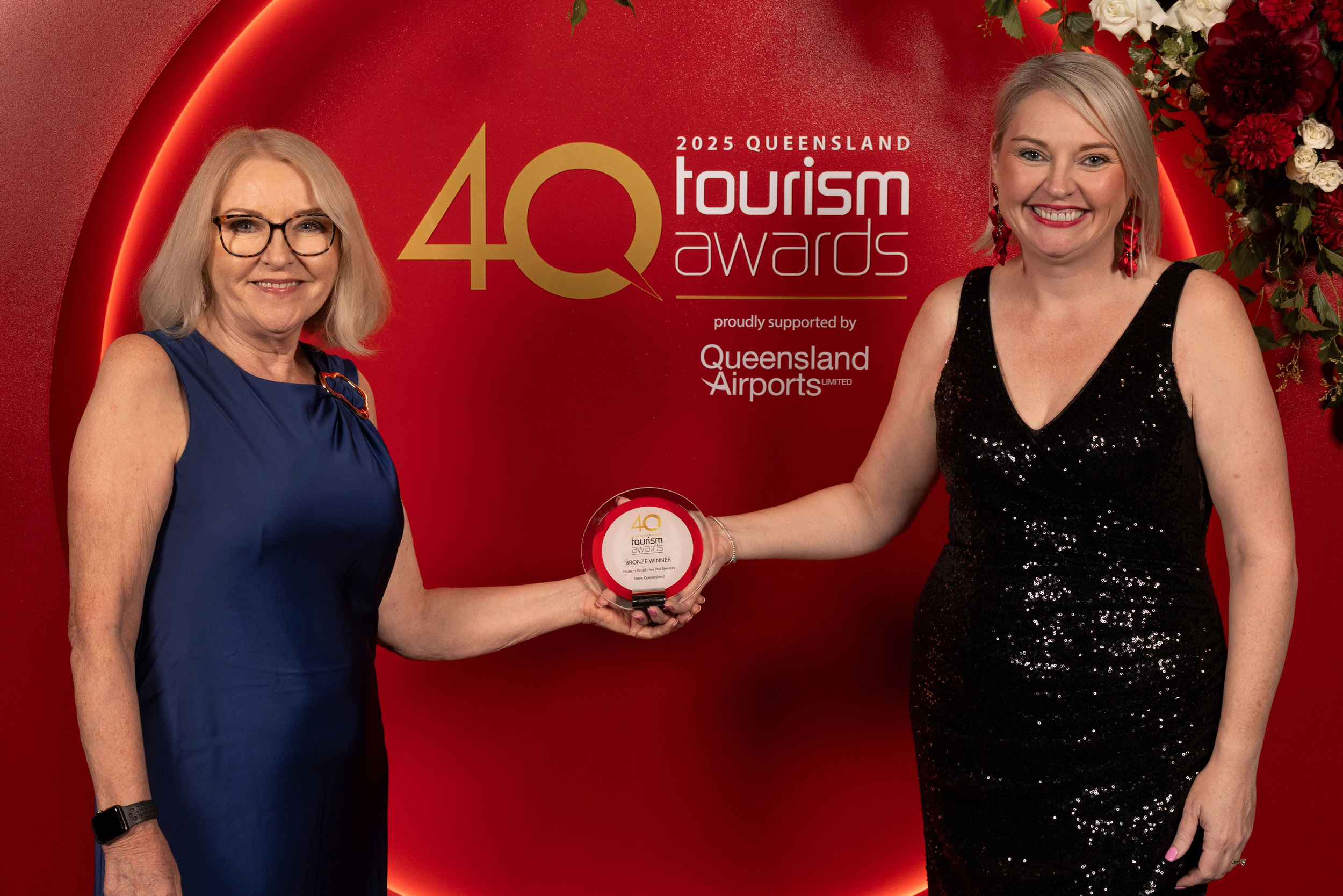 Two women stand in front of a "2023 Queensland Tourism Awards" backdrop, holding an award plaque together and smiling at the camera.