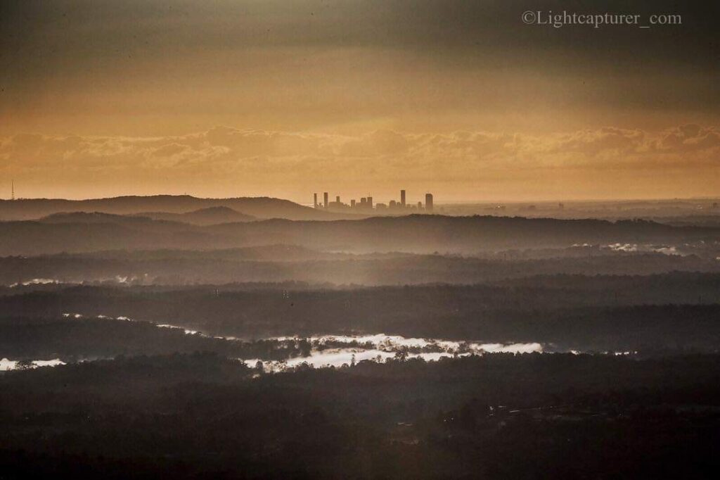 Distant city skyline under a golden sky, with layers of hills and reflective water in the foreground.