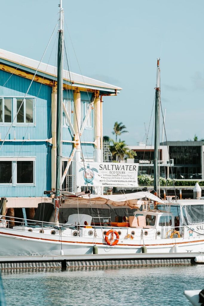 A white sailboat named Saltwater is docked near a blue building, with a sign on the boat advertising eco tours.