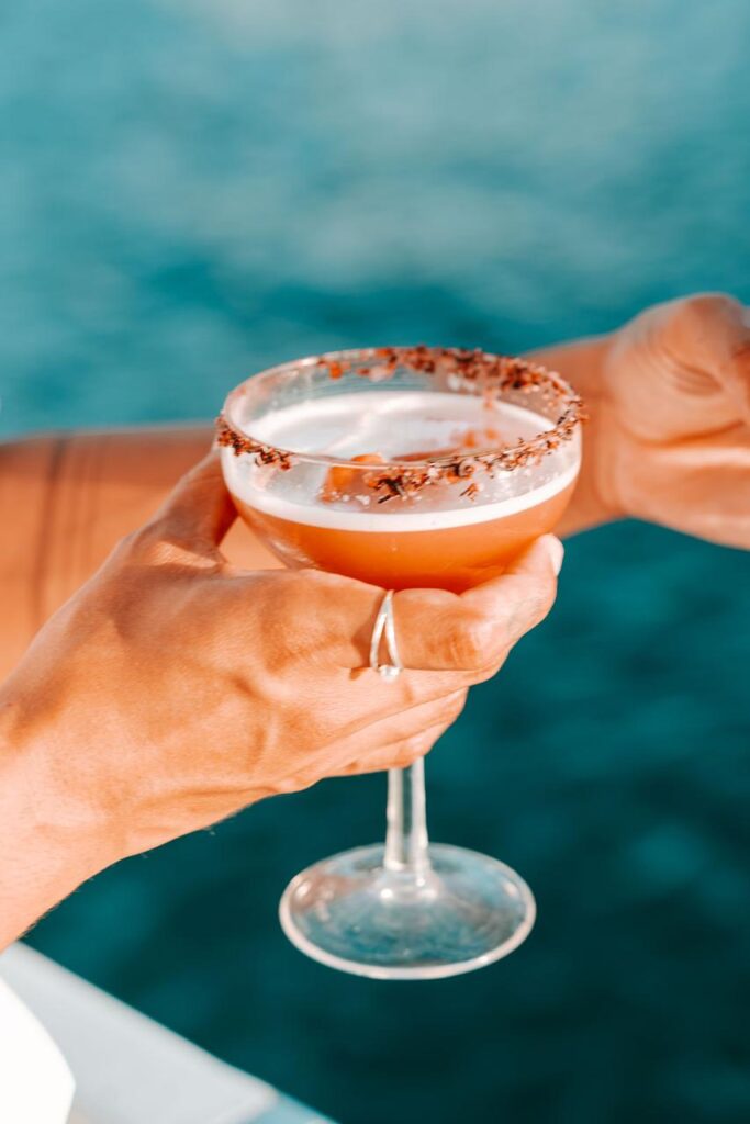 A person holding a cocktail in a coupe glass with a chocolate rim, against a blurred blue background.