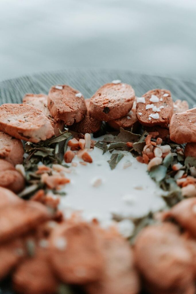 A close-up of biscotti slices arranged in a circle around a small pool of milk, with seeds and salt flakes scattered on top.