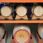 Wooden barrels of different sizes are stored on shelves, with three large barrels on the bottom row and six smaller barrels on the upper row.