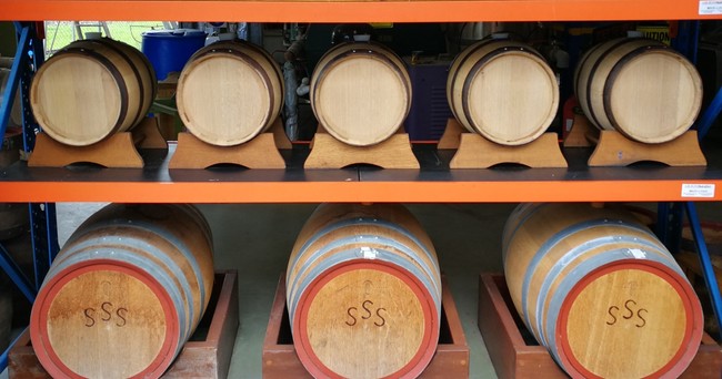 Wooden barrels of different sizes are stored on shelves, with three large barrels on the bottom row and six smaller barrels on the upper row.