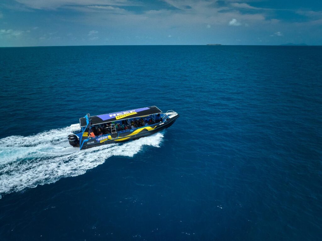 A speedboat with passengers travels across a vast expanse of blue ocean under a partly cloudy sky.