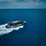 A speedboat with passengers travels across a vast expanse of blue ocean under a partly cloudy sky.