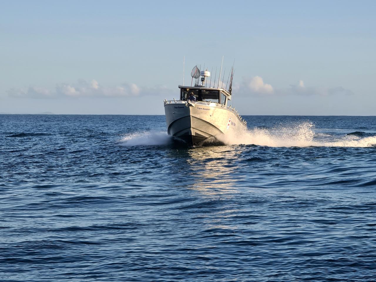 A white motorboat speeds across calm, blue ocean water under a clear sky, creating a trail of waves behind it.