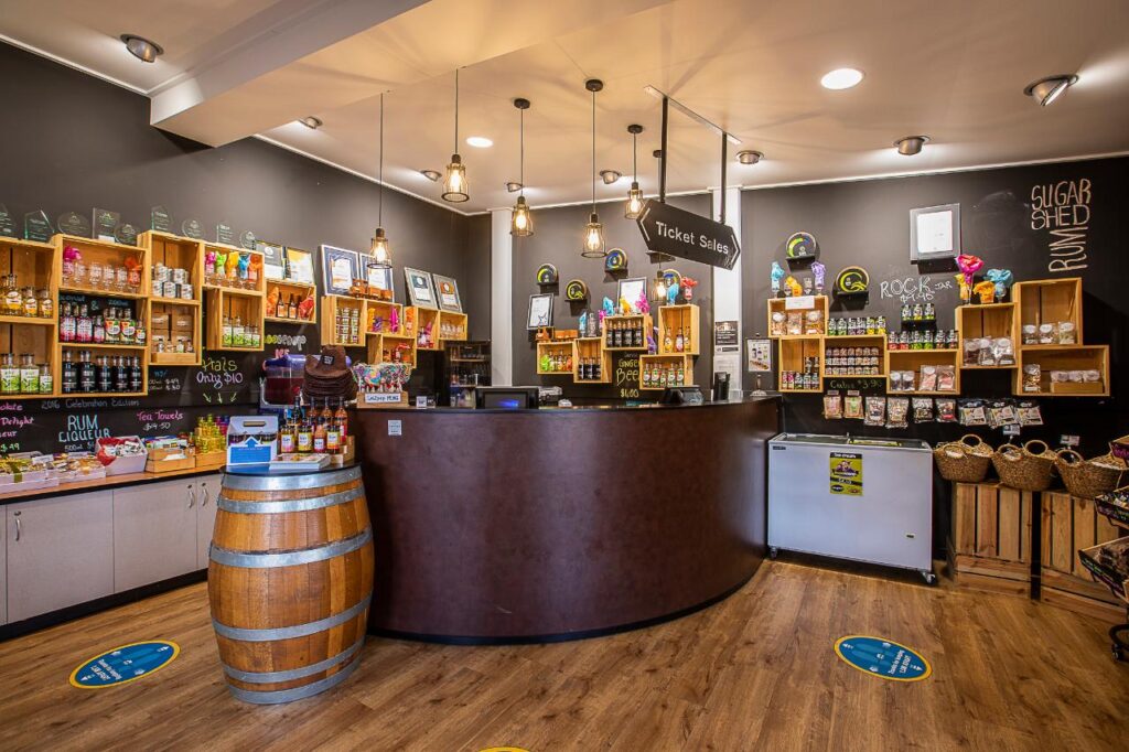 A shop interior with wooden shelves displaying jars, bottles, and products; a curved counter with a sign reading "Ticket Sales" and hanging lights above.