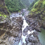 A rocky river gorge with steep, green hillsides and scattered boulders along the waterway.