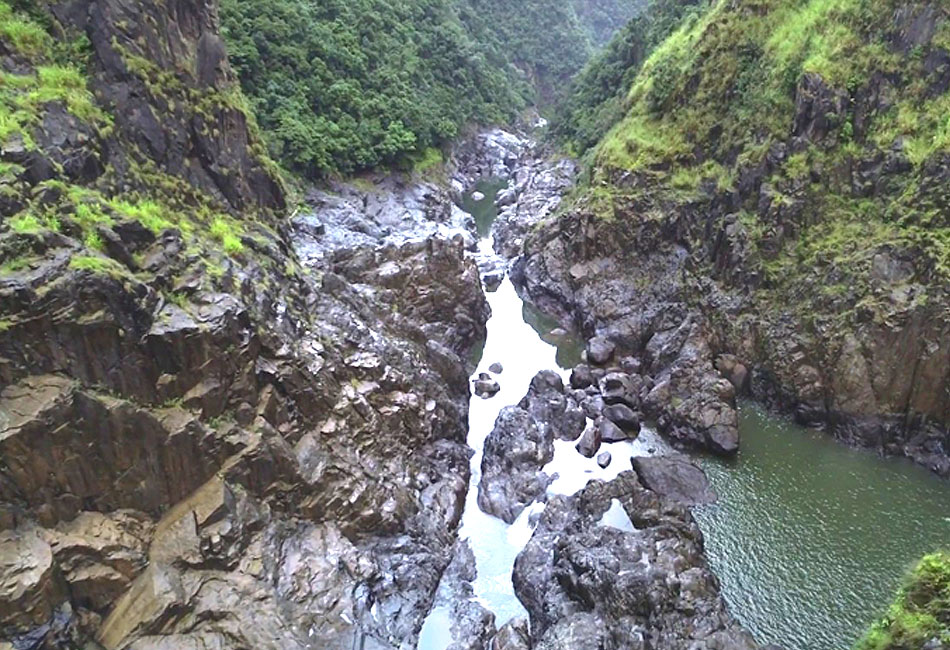 A rocky river gorge with steep, green hillsides and scattered boulders along the waterway.