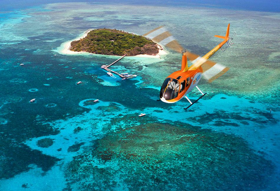 A bright orange helicopter flies over clear blue water near a small, lush island with boats anchored nearby.