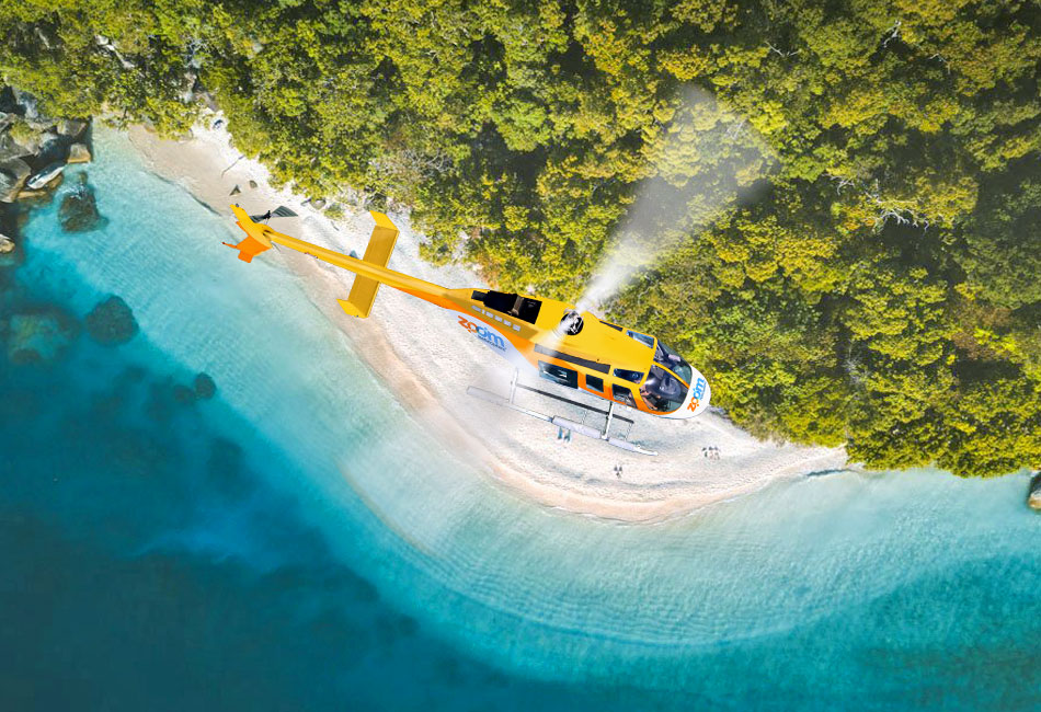 A yellow helicopter flies above a sandy beach with turquoise water and dense green trees, viewed from above.