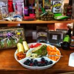A plate of assorted fruits and vegetables sits on a counter, surrounded by various packaged food items and condiments on shelves in the background.